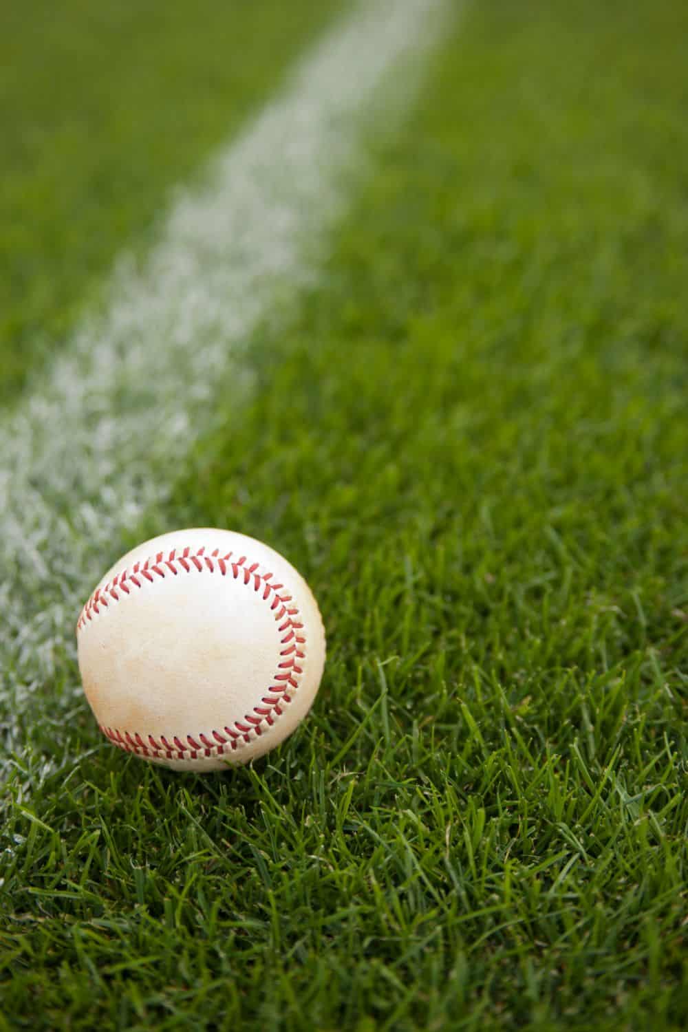 A baseball rests on vibrant green artificial turf next to a crisp white chalk line marking the sports field.