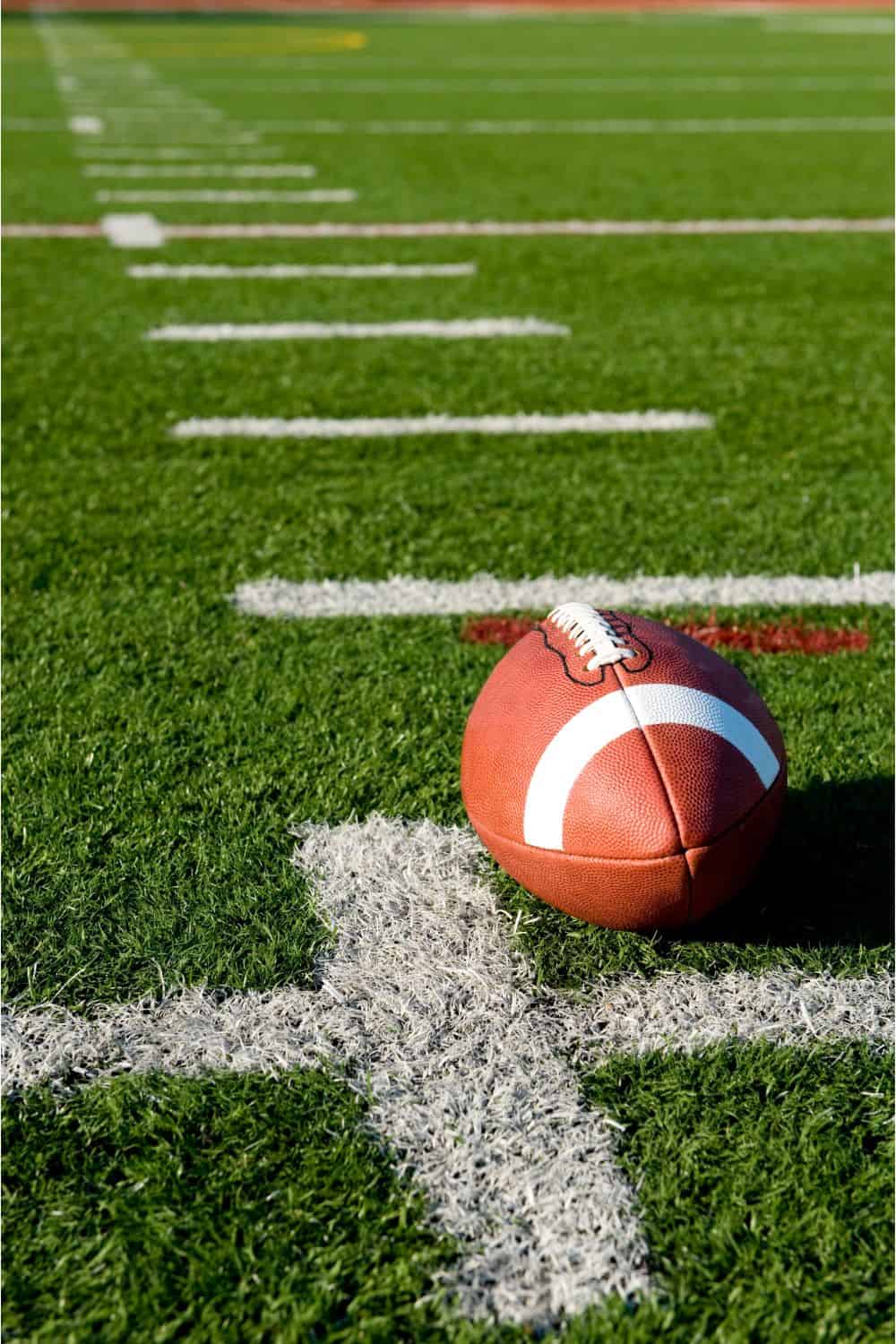 A football rests on a lush green field installed by a top-rated artificial grass installer in Apache Junction, AZ, next to a white yard line with more white lines visible across the turf.